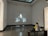 A person is sitting on a bench in a minimally decorated gallery room, facing a black-and-white movie projected onto the wall. The person appears to be watching the film intently. The room has high ceilings and some natural light coming in from the top.