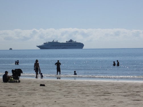 A vibrant photo of a group enjoying a sunny beach shore excursion with crystal-clear water and a cruise ship in the background.