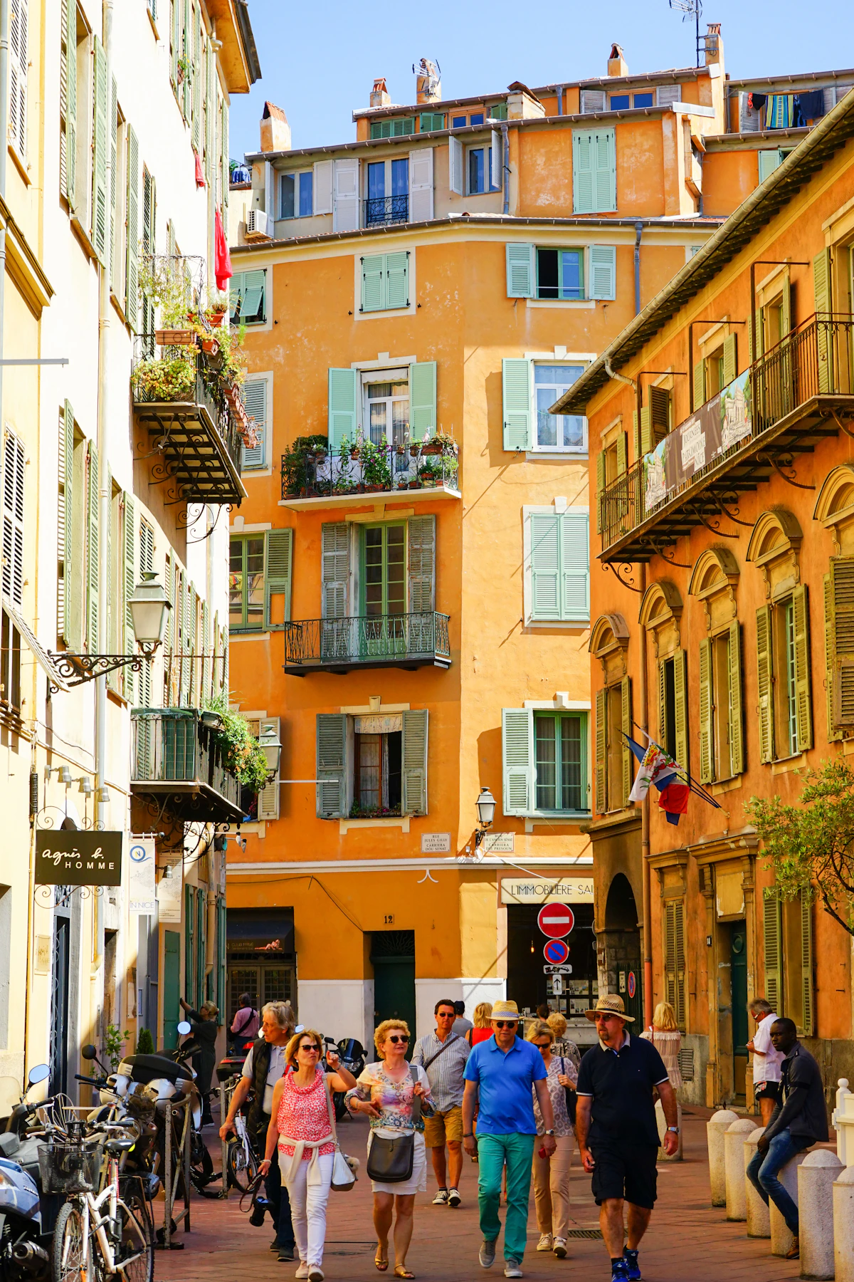 People walking between ochre buildings with green shutters in Vieux Nice