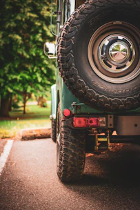 Close-up of a lifted side-by-side with big tires parked on a dirt trail surrounded by trees.