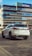 A white SUV is parked on a patterned pavement in front of a modern office building with glass windows and a KPMG logo. The vehicle is positioned at an angle showing the rear and side profiles.