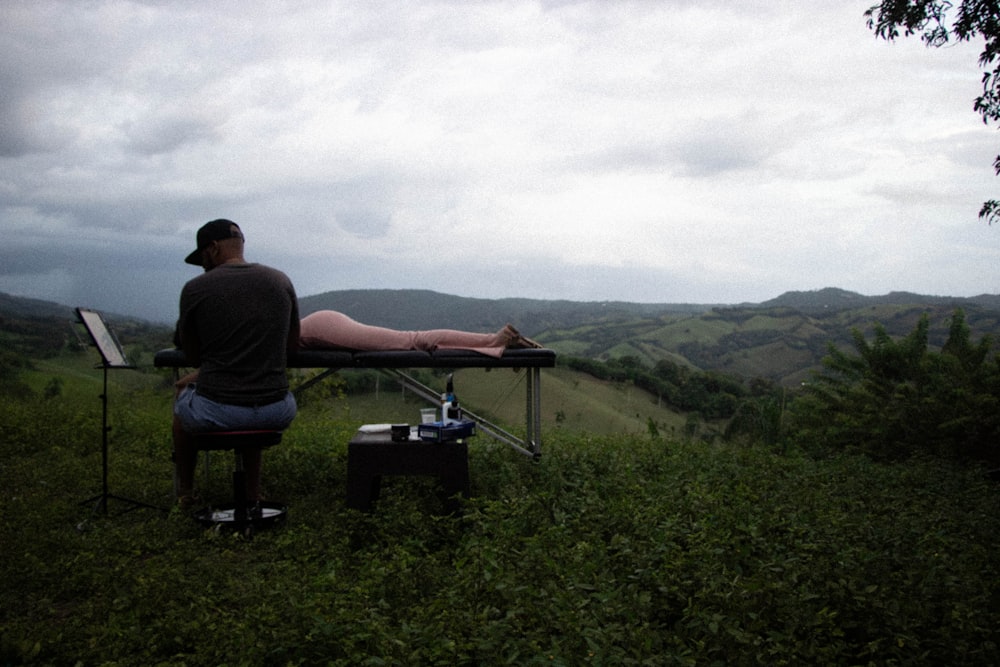 a man sitting on top of a bench in a field