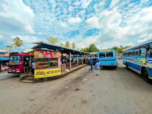 A bustling bus station with buses lined up and passengers boarding under a clear sky.