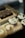 Cupcakes with creamy white frosting and red sprinkles are displayed alongside small cups with a caramel-colored layer and a chocolate brownie with visible nuts on a wooden tray.