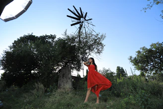 A model wearing a flowing red silk dress with delicate floral prints standing in a sunlit garden
