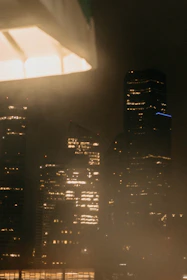 An evening cityscape with warm lights glowing through apartment windows, suggesting quiet stories within.
