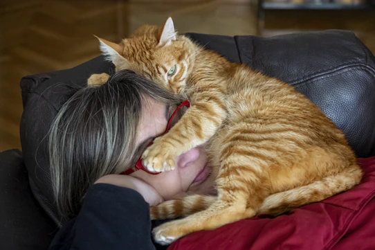 a woman laying on top of a couch next to a cat