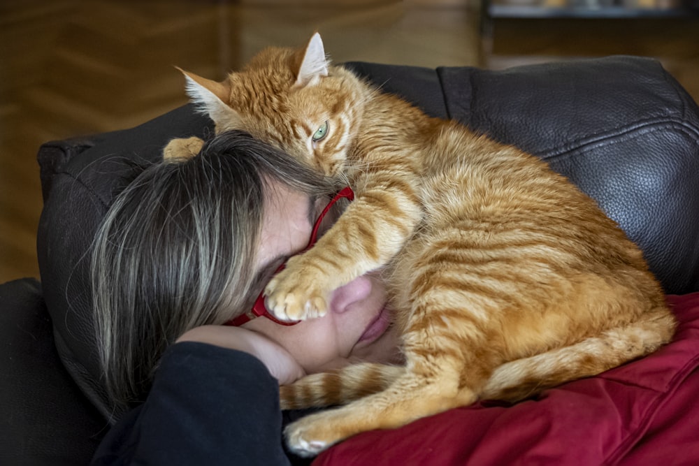 a woman laying on top of a couch next to a cat