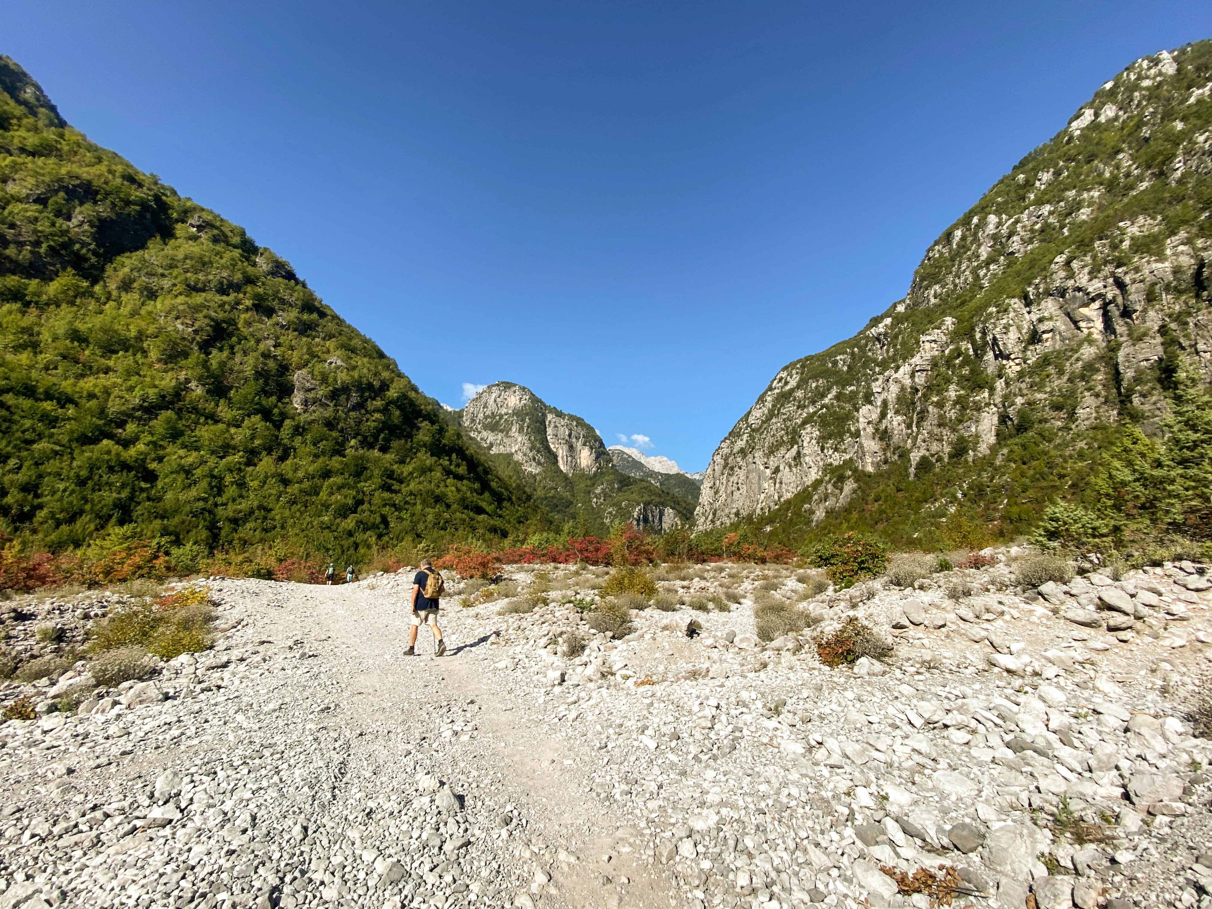 a person walking down a dirt road in the mountains, In the Albanian Alps