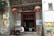An ancient temple entrance with traditional Chinese architecture. Two large red lanterns hang above the doorway, flanked by historical and informational plaques. Two women are seated at a table outside, engaged in conversation.