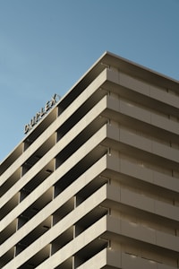A multi-story building features a series of uniform balconies. The word 'DUPLEX' is visible on the top corner, indicating the building's name or type of residence. The architecture is modern and minimalist, with a smooth, geometric facade against a clear blue sky.