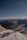 A telecommunications tower stands on a snow-covered mountain peak with rugged mountains and a clear blue sky in the background, creating a contrast between technology and nature.