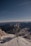 A telecommunications tower stands on a snow-covered mountain peak with rugged mountains and a clear blue sky in the background, creating a contrast between technology and nature.