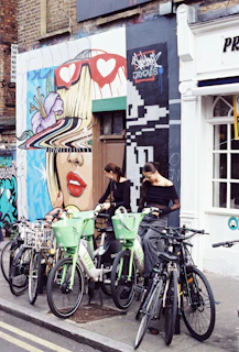 A vibrant urban mural backdrop with a Lumina Apparel tote bag hanging from a bicycle handle.