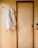A white padded jacket is hanging on a small wooden peg mounted on a wooden wall. Next to it is a wooden sliding door with a black handle, matching the wood texture and color of the wall. The setting has a minimalist feel with light wood tones dominating the scene.