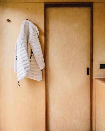 A sleek black and white athletic jacket hanging on a minimalist wooden hanger against a plain white wall.