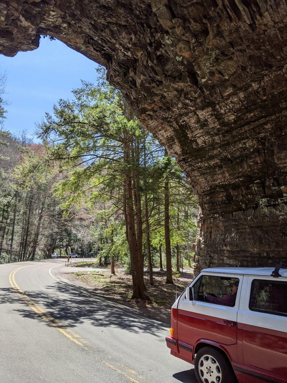 a red van is parked under a large rock