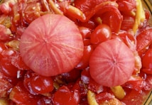 A close-up view of a colorful and textured salad consisting of vibrant red tomatoes, peeled pink radishes, and sliced yellow peppers. The mixture appears fresh and juicy, with a glistening appearance due to a light dressing or natural moisture.