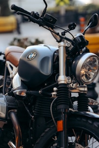 A close-up view of a motorcycle showcasing intricate details like the handlebars, tank, and headlight in sharp focus. The motorcycle exhibits a classic aesthetic with metallic and chrome elements, along with an emblem displayed prominently on the tank.