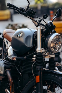 A close-up view of a motorcycle showcasing intricate details like the handlebars, tank, and headlight in sharp focus. The motorcycle exhibits a classic aesthetic with metallic and chrome elements, along with an emblem displayed prominently on the tank.