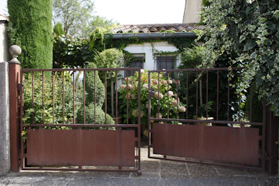 A galvanized double wire mesh garden gate partially open revealing a vibrant garden path beyond.