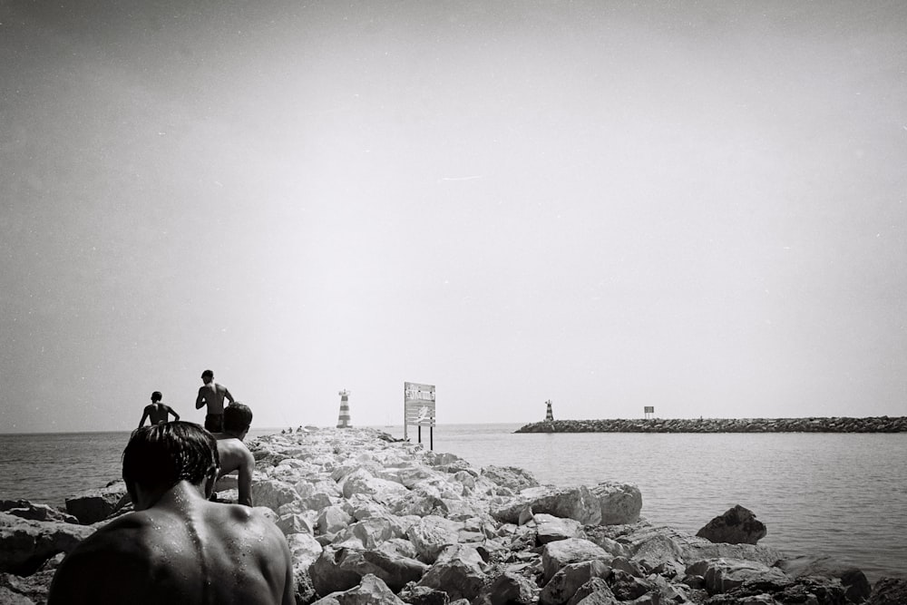 a black and white photo of people sitting on rocks near a body of water