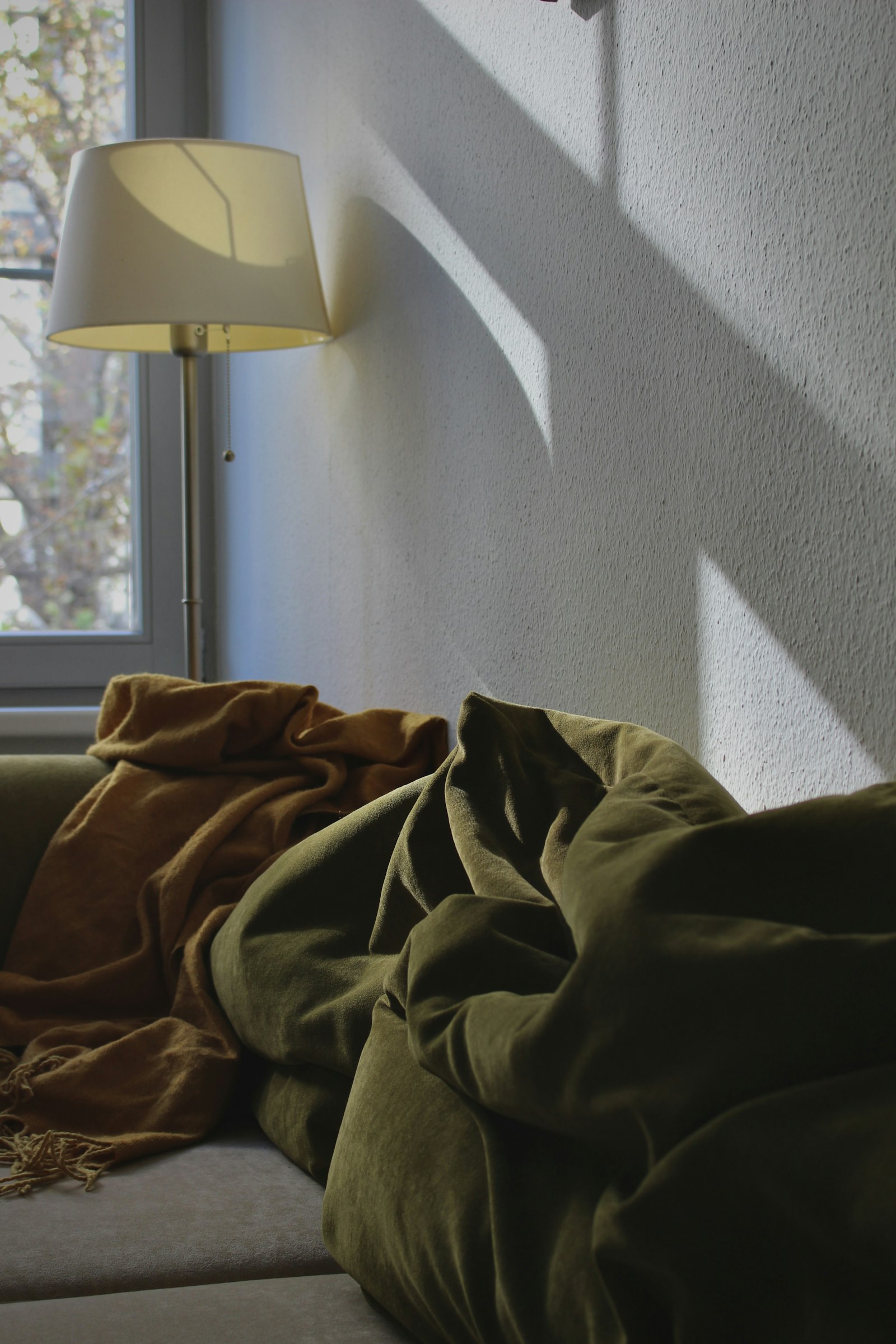 Empty couch in soft afternoon light with a mustard throw and floor lamp, intimate domestic interior