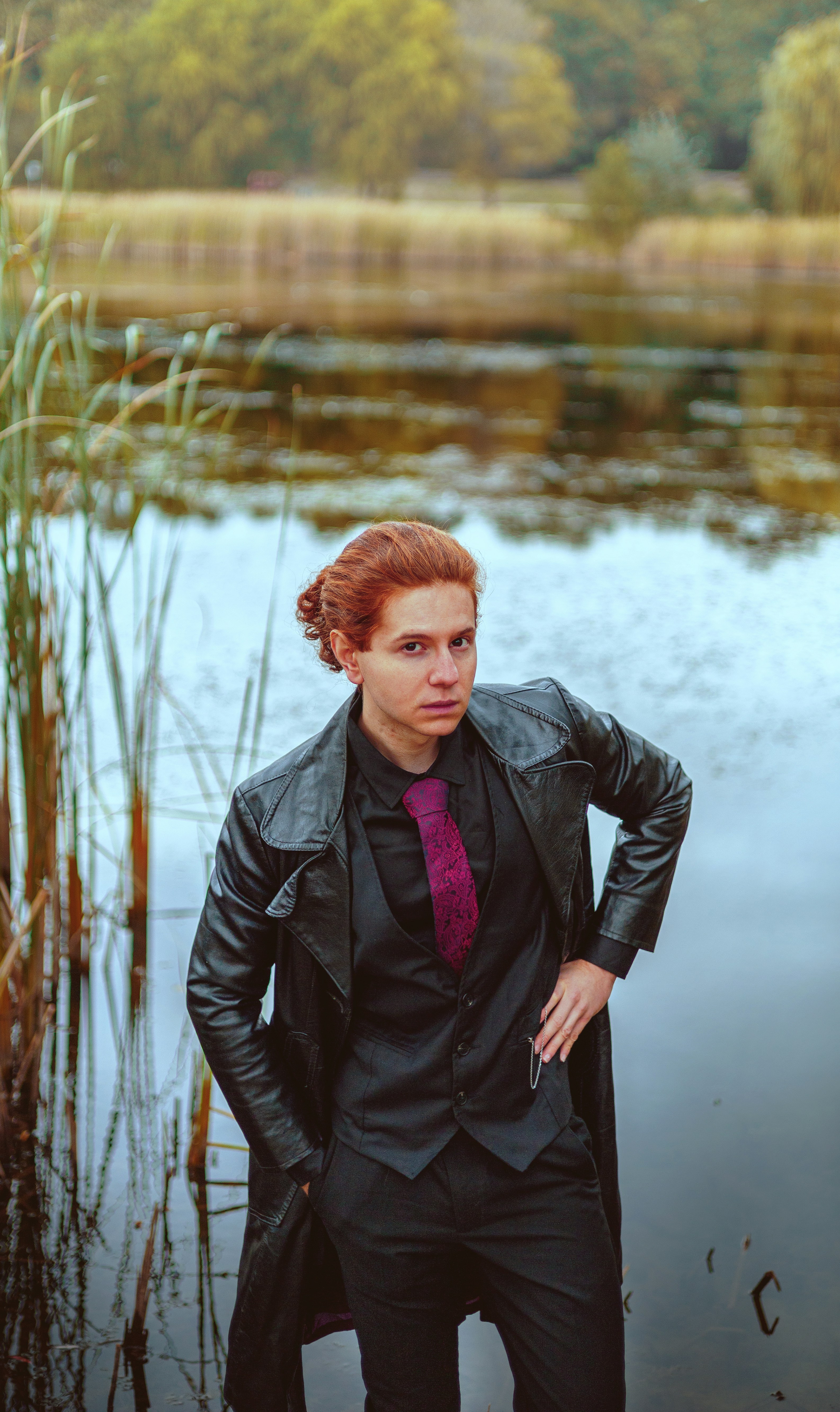 a man in a suit and tie standing in front of a lake