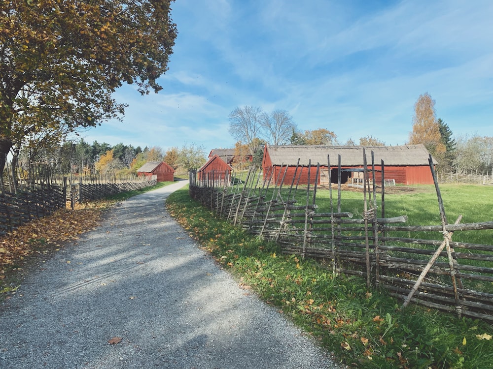 a country road with a fence and a barn in the background