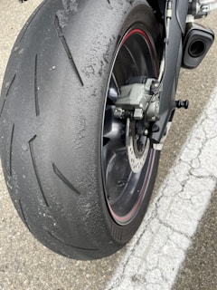 A close-up view of a motorcycle rear tire showing significant wear and rubber debris build-up from usage. The tire features a tread pattern designed for road use and is accompanied by a visible disc brake system.