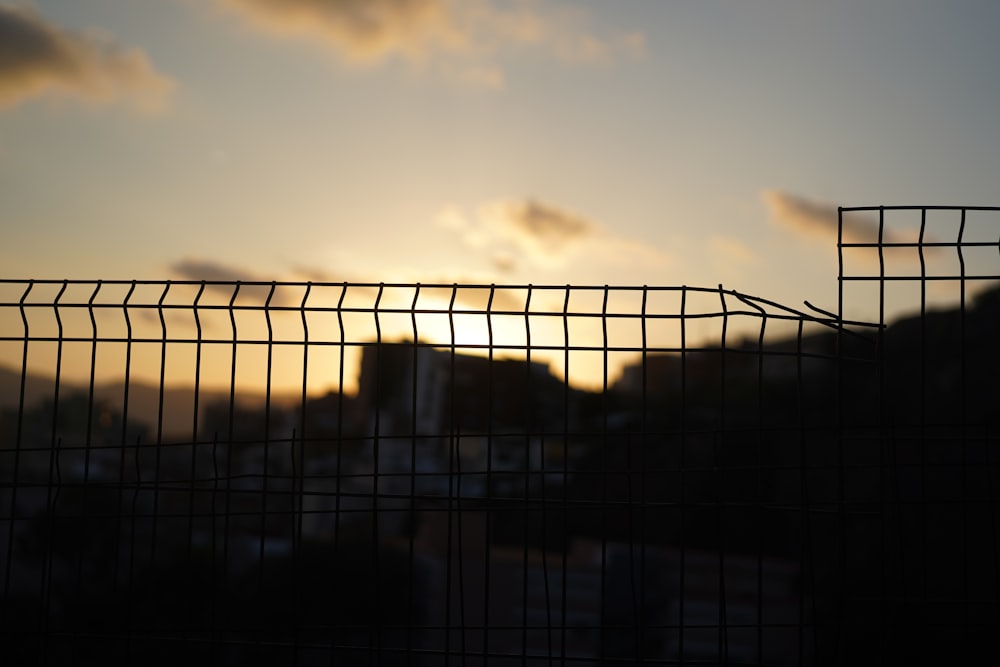 the sun is setting behind a wire fence