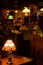 A dimly lit antique shop with various vintage objects, including lamps with stained glass and colored shades. Shelves are filled with decorative items and furniture, creating a nostalgic and cozy atmosphere.