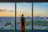Smiling businesswoman standing by a window overlooking a global city skyline at dusk.