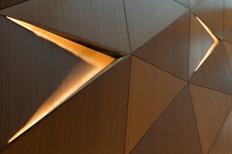 Geometric panels with a wood-like texture feature elongated triangular light slots. The arrangement creates a contemporary, abstract pattern with warm lighting highlights.