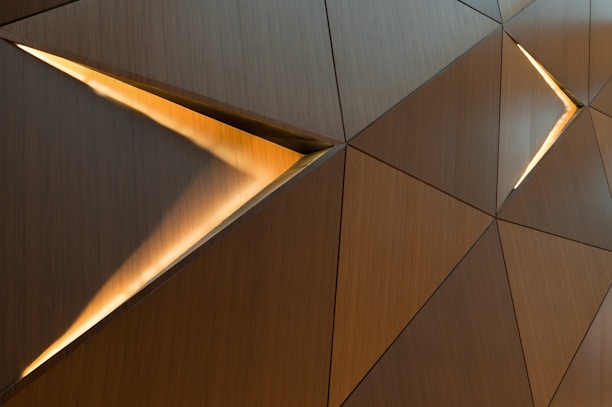 Geometric panels with a wood-like texture feature elongated triangular light slots. The arrangement creates a contemporary, abstract pattern with warm lighting highlights.