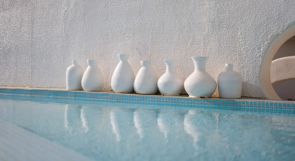 a row of white vases sitting next to a swimming pool