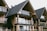 A series of modern wooden houses with large glass windows and triangular, black shingled roofs. The architecture features balconies with glass railings, creating a sleek and contemporary appearance.