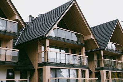 A series of modern wooden houses with large glass windows and triangular, black shingled roofs. The architecture features balconies with glass railings, creating a sleek and contemporary appearance.