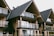 A series of modern wooden houses with large glass windows and triangular, black shingled roofs. The architecture features balconies with glass railings, creating a sleek and contemporary appearance.