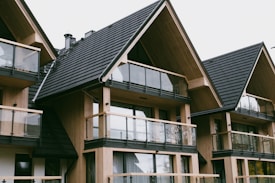 A series of modern wooden houses with large glass windows and triangular, black shingled roofs. The architecture features balconies with glass railings, creating a sleek and contemporary appearance.