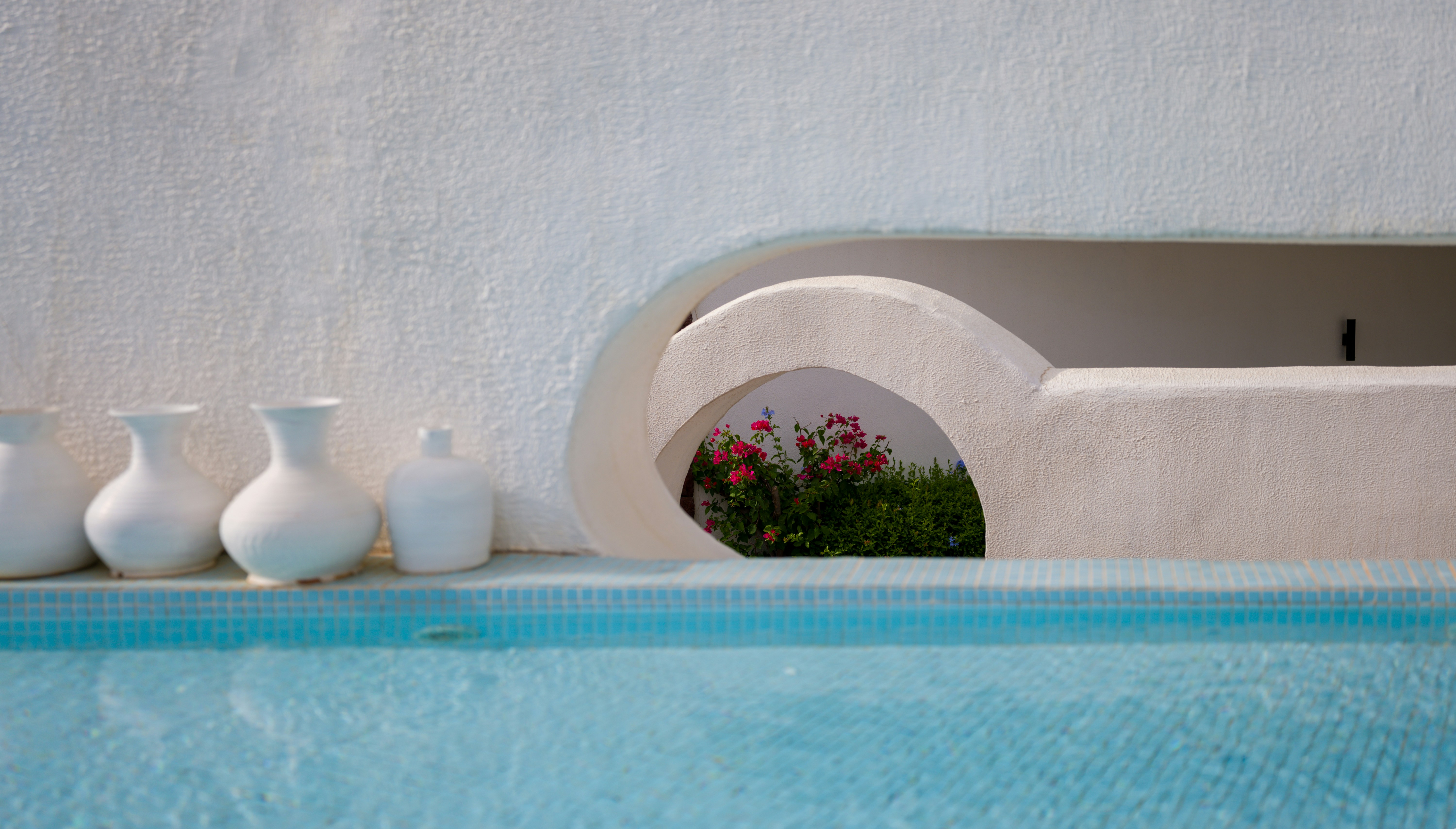 The white ceramic jars beside the pool and the flowers in the distance can be seen in the hollows on the wall of the pool.