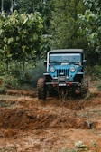 A rugged off-road vehicle climbing a rocky mountain trail surrounded by greenery.