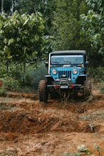 A muddy off-road truck equipped with heavy-duty accessories driving through a forest trail.