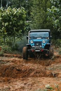 A rugged jeep climbing a muddy mountain trail surrounded by lush greenery.