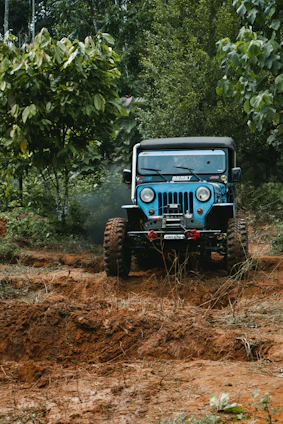 A muddy off-road truck equipped with heavy-duty accessories driving through a forest trail.
