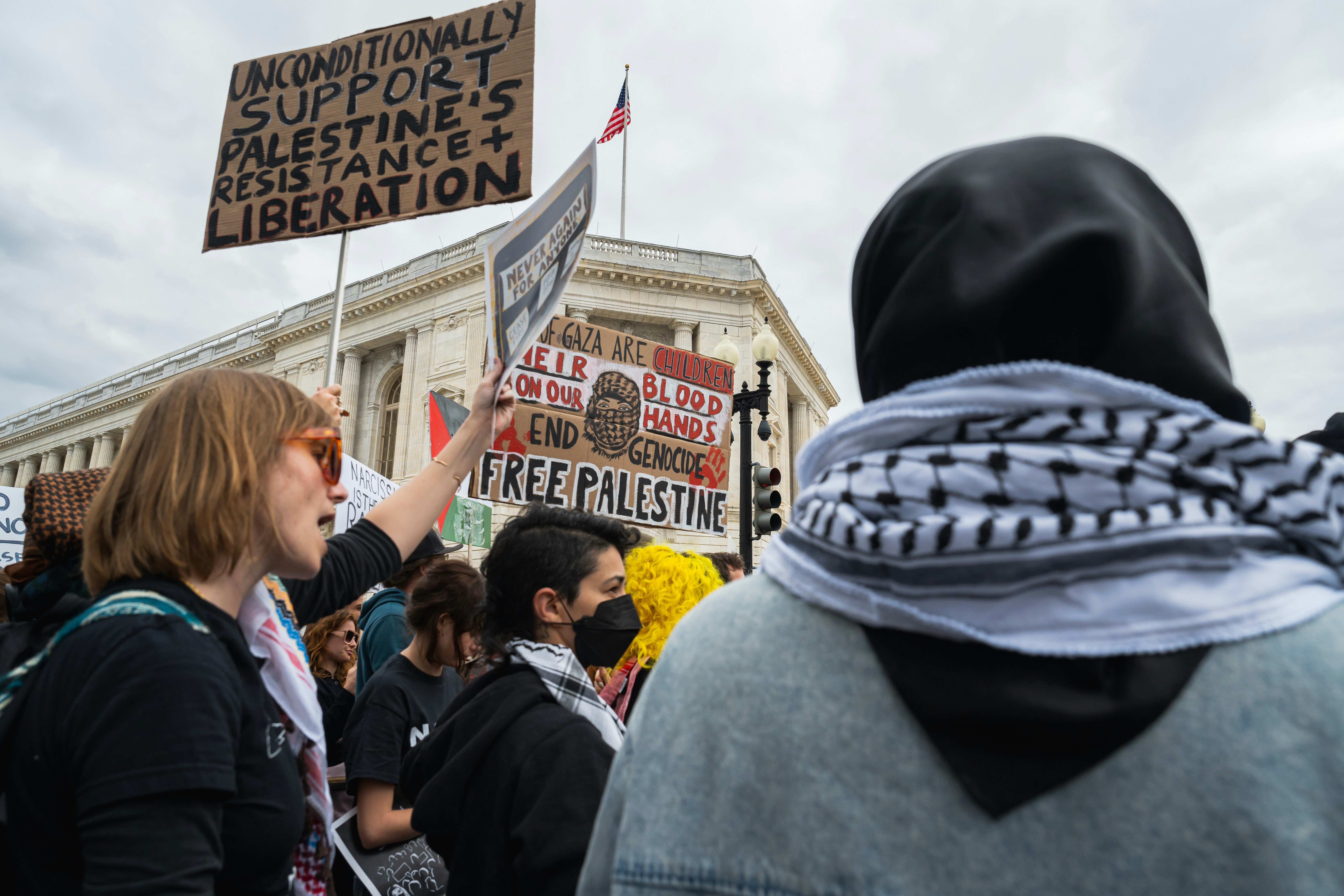 a group of people holding signs in front of a building, Their Blood On Our Hands