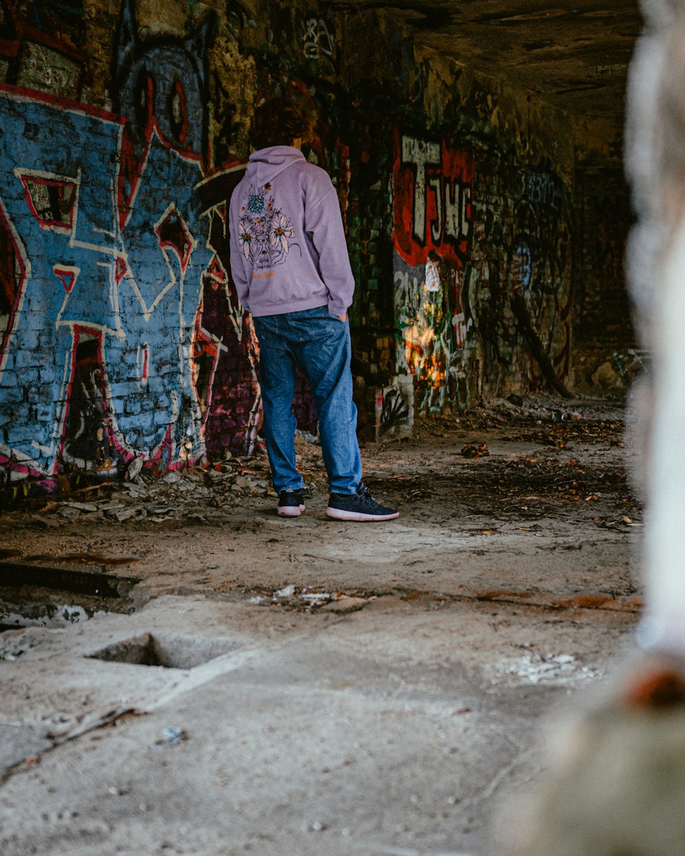 a man in a purple jacket is standing in a room with graffiti on the walls