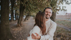 The couple walking down a tree-lined path, smiling warmly at each other.