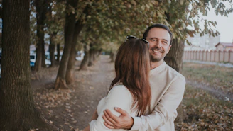 The couple walking down a tree-lined path, smiling warmly at each other.