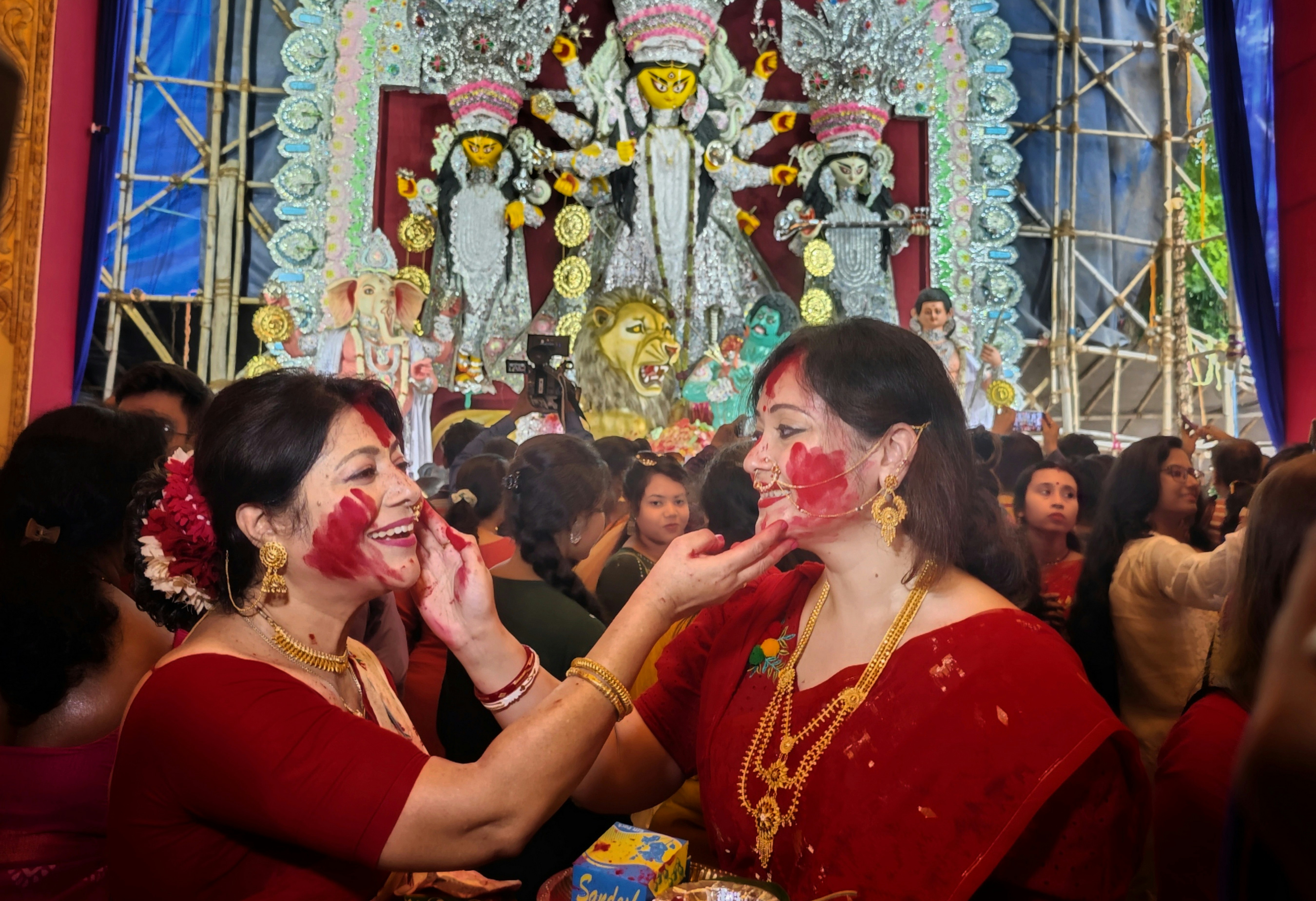 Women celebrating Sindoor Khela with vibrant red sindoor powder in bright natural light